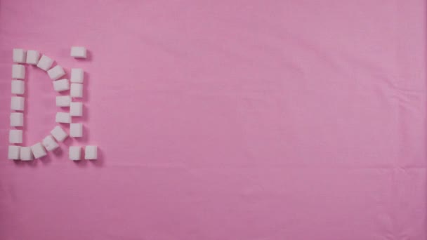 Das Wort "Diabetiker" ist mit raffinierten Zuckerwürfeln auf rosa Hintergrund unterlegt. Konzept der Karies — Stockvideo