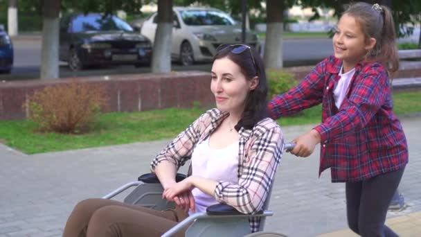 Meisje helpt moeder aan een gehandicapte persoon in een rolstoel op de wandeling trage mo — Stockvideo