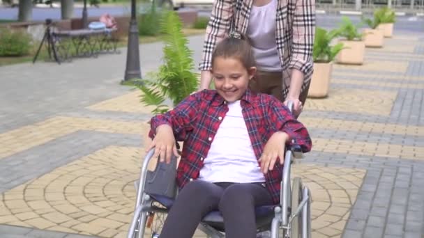 Mädchen fährt glücklich Teenager im Rollstuhl im Sommer park.slow mo — Stockvideo