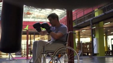 Engelli bir tekerlekli sandalyede bir adam kum torbasına eldiven ile spor salonunda atıyor..