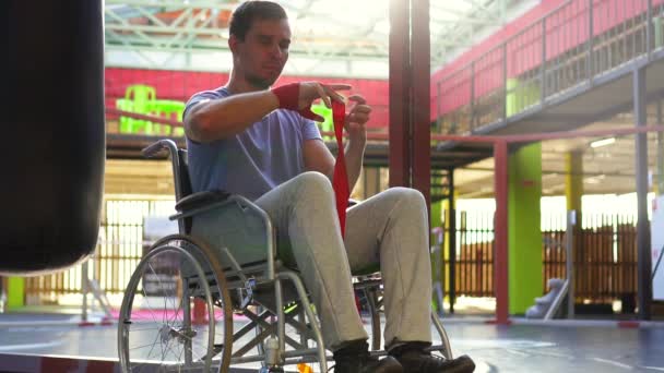 Hombre con una discapacidad en una silla de ruedas herida cintas de boxeo en sus manos. — Vídeos de Stock