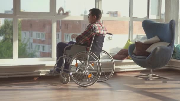 Handikappade mannen sitter vid fönstret i rullstol — Stockvideo