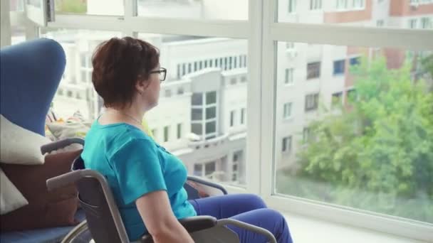 Женщина с инвалидностью в инвалидном кресле подъезжает к окну — стоковое видео