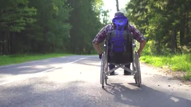 Homem com deficiência em uma cadeira de rodas passeios de viajantes na estrada — Vídeo de Stock