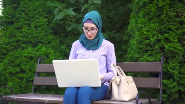 Elegante y atractiva joven musulmana en un hijab trabajando en el ordenador portátil en el parque — Vídeos de Stock