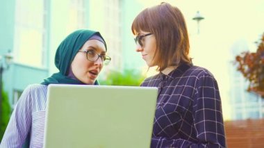 Tesettür ve arkadaşı parkta sunflare sohbet dizüstü bilgisayar ile Müslüman kız öğrenci. Yavaş mo