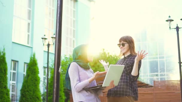 Estudante muçulmano no hijab e sua amiga estão felizes olhando para o sol laptop. — Vídeo de Stock