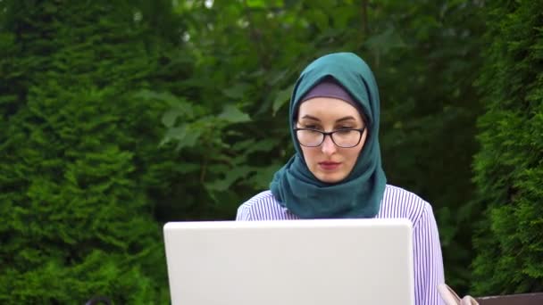 Κομψή και ελκυστική νεαρή μουσουλμάνα σε ένα hijab που εργάζονται για το laptop στο πάρκο. Κοντινό πλάνο — Αρχείο Βίντεο