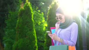 Genç Müslüman kadının telefon kullanarak alışveriş sonra elinde hijab torbalarda. Sunflare