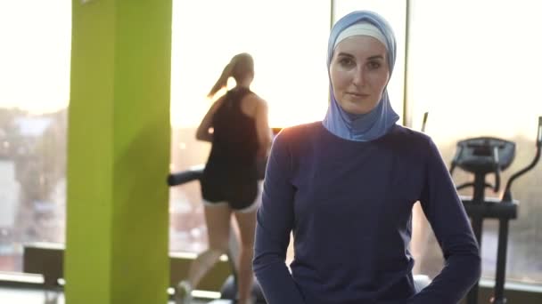 Porträtt av en ung muslimsk tjej i en halsduk i en elegant gym, sunflare. Långsamma mo — Stockvideo