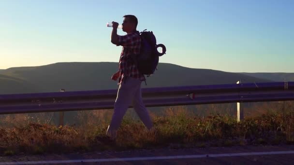 Homem viaja com uma mochila atrás dele está na estrada, slow mo — Vídeo de Stock