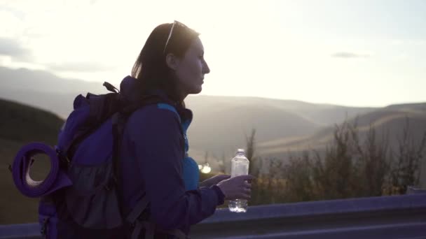 Retrato chica viajero con una mochila va en el camino y bebe agua — Vídeo de stock