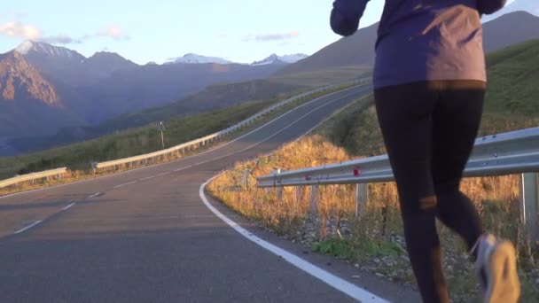 Sportlerin läuft bei Sonnenuntergang auf der Straße in die Berge aus nächster Nähe — Stockvideo