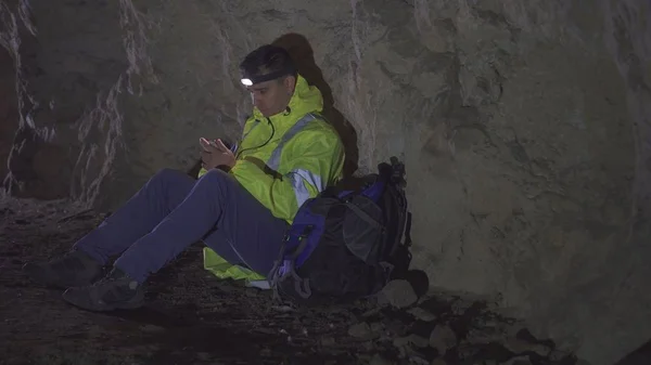 Verlorener Tourist mit Rucksack benutzt das Telefon in der Höhle — Stockfoto