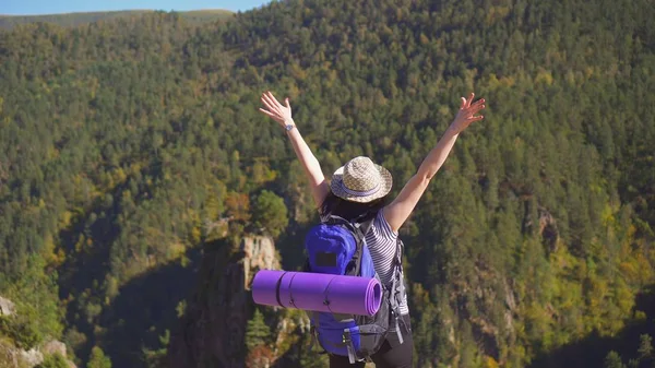 Kız turistik bir sırt çantası içinde bir şapka ile dağlarda ellerini kaldırdı