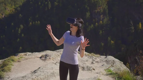 vr Gözlüklü kız dağlarda bir uçurumun kenarında duran şaşırttı