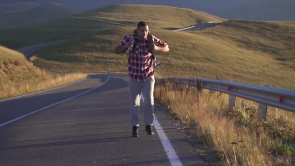 Hombre turista con una mochila detrás va en el camino a las montañas — Vídeo de stock