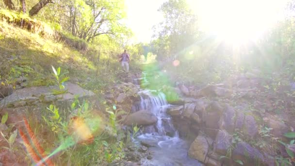 Man toeristische met rugzak gaat over de rivier berg — Stockvideo