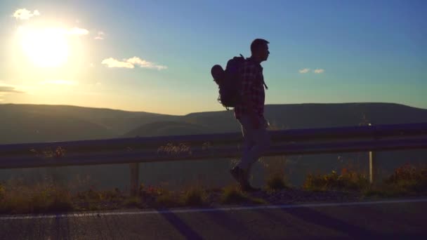 Homem viajante com uma grande mochila atrás e uma garrafa na mão está na estrada — Vídeo de Stock