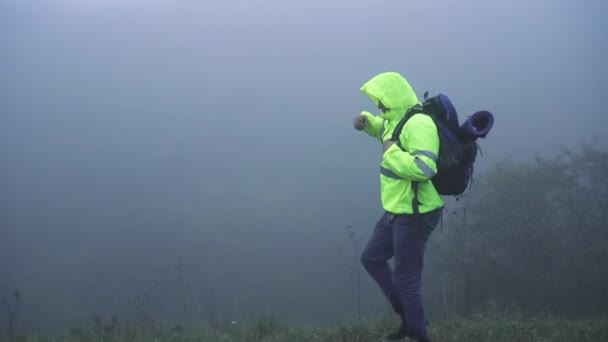 Homme touriste en gilet de signalisation à capuche avec sac à dos marchant dans le brouillard seul, gros plan — Video