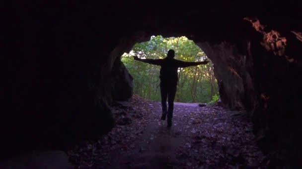 Touriste homme avec sac à dos court hors de la grotte sombre et lève les mains, lent mo — Video