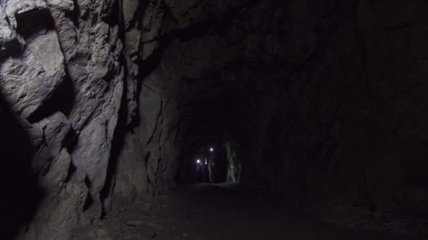 Ragazza e l'uomo turisti passano attraverso una grotta oscura profonda con una torcia elettrica — Video Stock