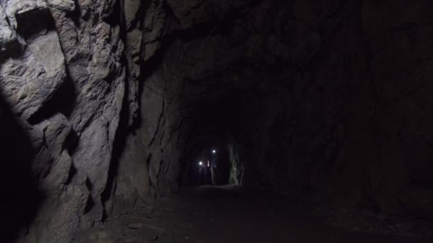 Menina e homem turistas atravessam uma caverna profunda escura com uma lanterna — Vídeo de Stock