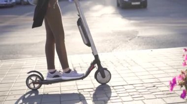 Wooman bir elektrikli scooter güneşli bir şehir sürmek.