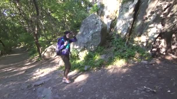 Chica turista con mochila entra en una profunda cueva oscura en el bosque — Vídeo de stock