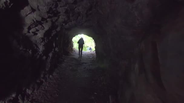 Meisje toerist met een rugzak met een zaklamp op zijn voorhoofd komt in een donkere grot — Stockvideo