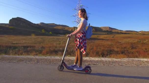 Mladá dívka jezdí elektrický skútr na silnici, slunce — Stock video