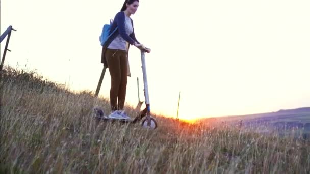 Chica montando en scooter eléctrico en una ladera de montaña al atardecer, lento mo — Vídeos de Stock