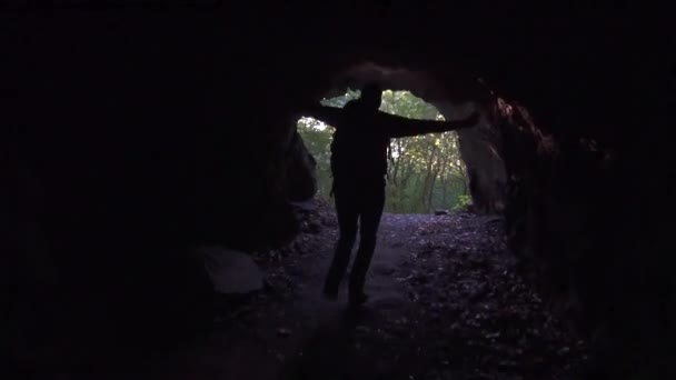 Man tourist with backpack runs out of the dark cave and raises his hands up — Stockvideo