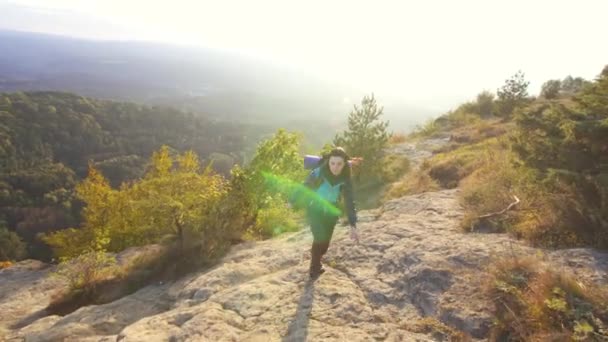 Молодая туристка с рюкзаком поднимается на гору и поднимает руки от радости — стоковое видео