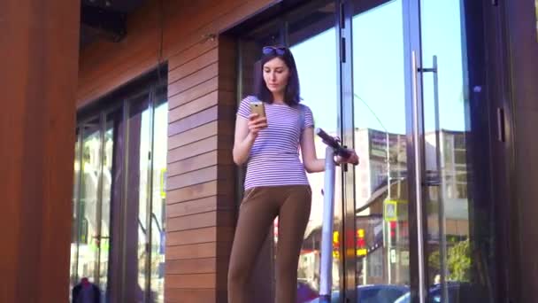 Chica joven utiliza el teléfono al lado del scooter eléctrico — Vídeo de stock