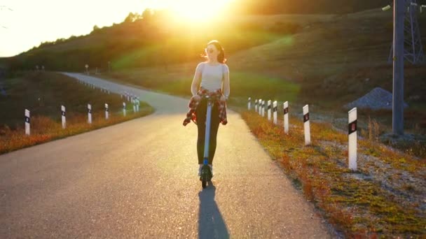 Jonge vrouw die een e-scooter rijden op zonsondergang achter, langzame mo — Stockvideo