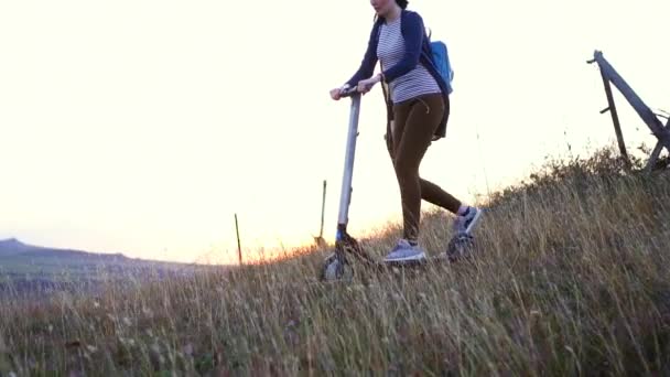 Chica joven montando un scooter eléctrico en una montaña al atardecer, lento mo — Vídeos de Stock