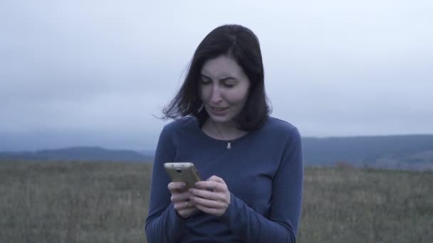 Ung kvinna läser dåliga nyheter på en mobiltelefon i dåligt väder, långsamma mo — Stockvideo