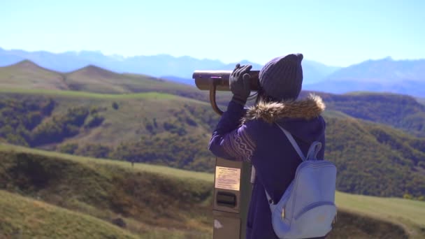 Chica turística en la plataforma de observación mira a las montañas a través de prismáticos, lento mo — Vídeo de stock
