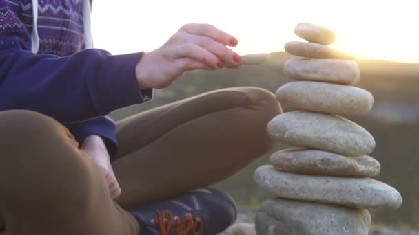Дівчина збирає піраміду з каменів крупним планом на заході сонця — стокове відео