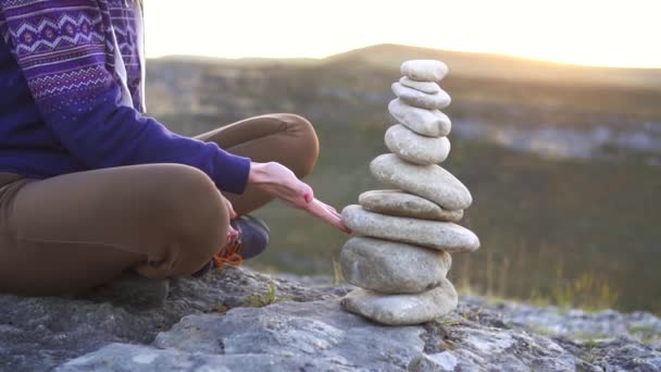 Mädchen lässt bei Sonnenuntergang eine Pyramide aus Steinen aus nächster Nähe fallen — Stockvideo