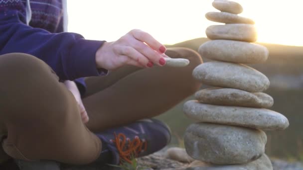 Dívka sbírá a pyramida kamenů zblízka při západu slunce, pomalé mo — Stock video