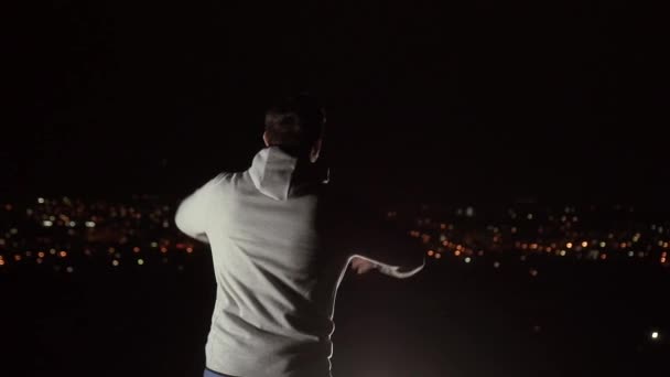 Человек с распростертыми объятиями ночью с видом на город, медленное время — стоковое видео