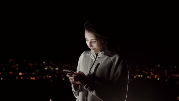 Chica bonita utiliza el teléfono por la noche en el fondo de la ciudad de la noche, lento mo — Vídeos de Stock