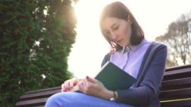 Kız açık havada günbatımında banktaoturuyor bir kitapla