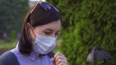 Günbatımında bir bankta bir telefon ile koruyucu tıbbi maske yüzünde hasta bir kız portresi