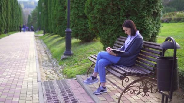 Chica leyendo un libro sentado en un banco — Vídeos de Stock