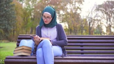 Sevimli öğrenci Müslüman kız hijab günbatımında bir tezgah üzerine bir kitap okuma