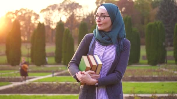 Muslim student with books in hijab in the park at sunset — Stock Video