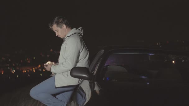 Мужчина водитель на фоне ночного города использует смартфон — стоковое видео